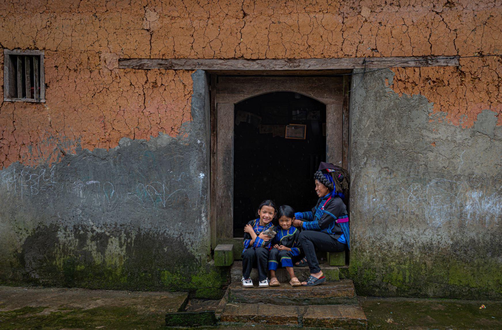 Bên bậu cửa nhà trình tường truyền thống của người Hà Nhì, Y Tý. Trang phục của người Hà Nhì đen có màu xanh đặc trưng.