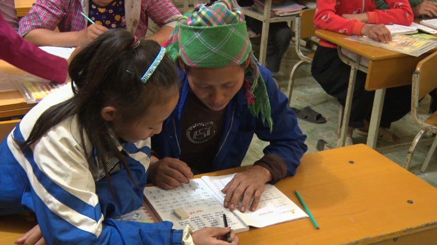 Một học sinh hướng dẫn mẹ đánh vần, tập viết tại lớp xóa mù chữ. Ảnh: Trịnh Hổ. 2.jpg