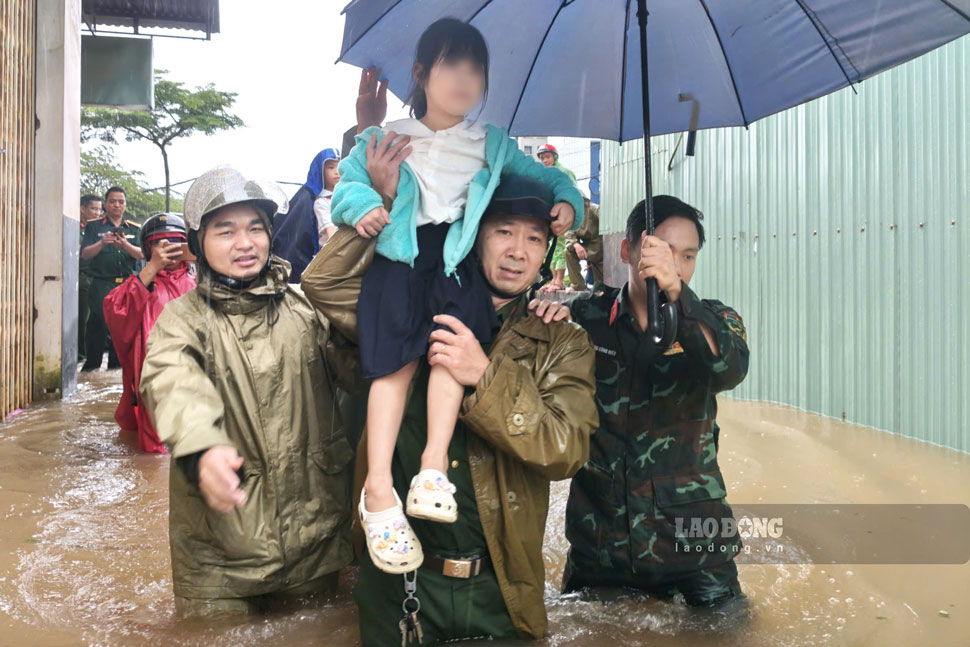 Lực lượng chức năng hỗ trợ đưa bé gái qua khu vực ngập. Ảnh: Lê Tiền
